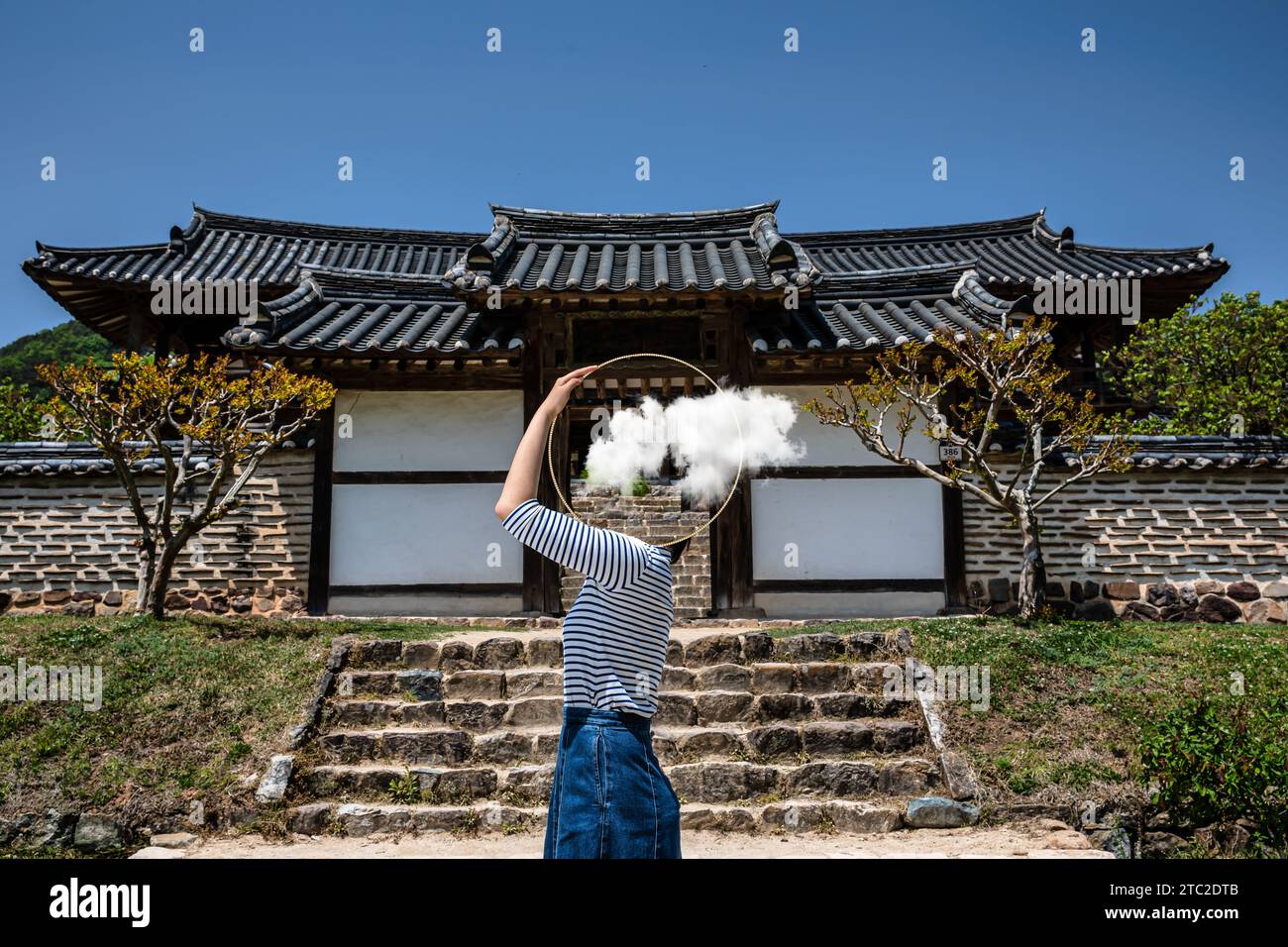 Surrealismo con una donna che tiene uno specchio e copre il volto di fronte alla vecchia casa tradizionale, con uno sfondo trasparente dietro lo specchio Foto Stock
