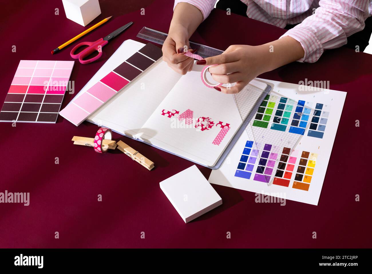 Mano di una donna che decora un diario con sfondi e oggetti di scena di colore Viva Magenta Foto Stock