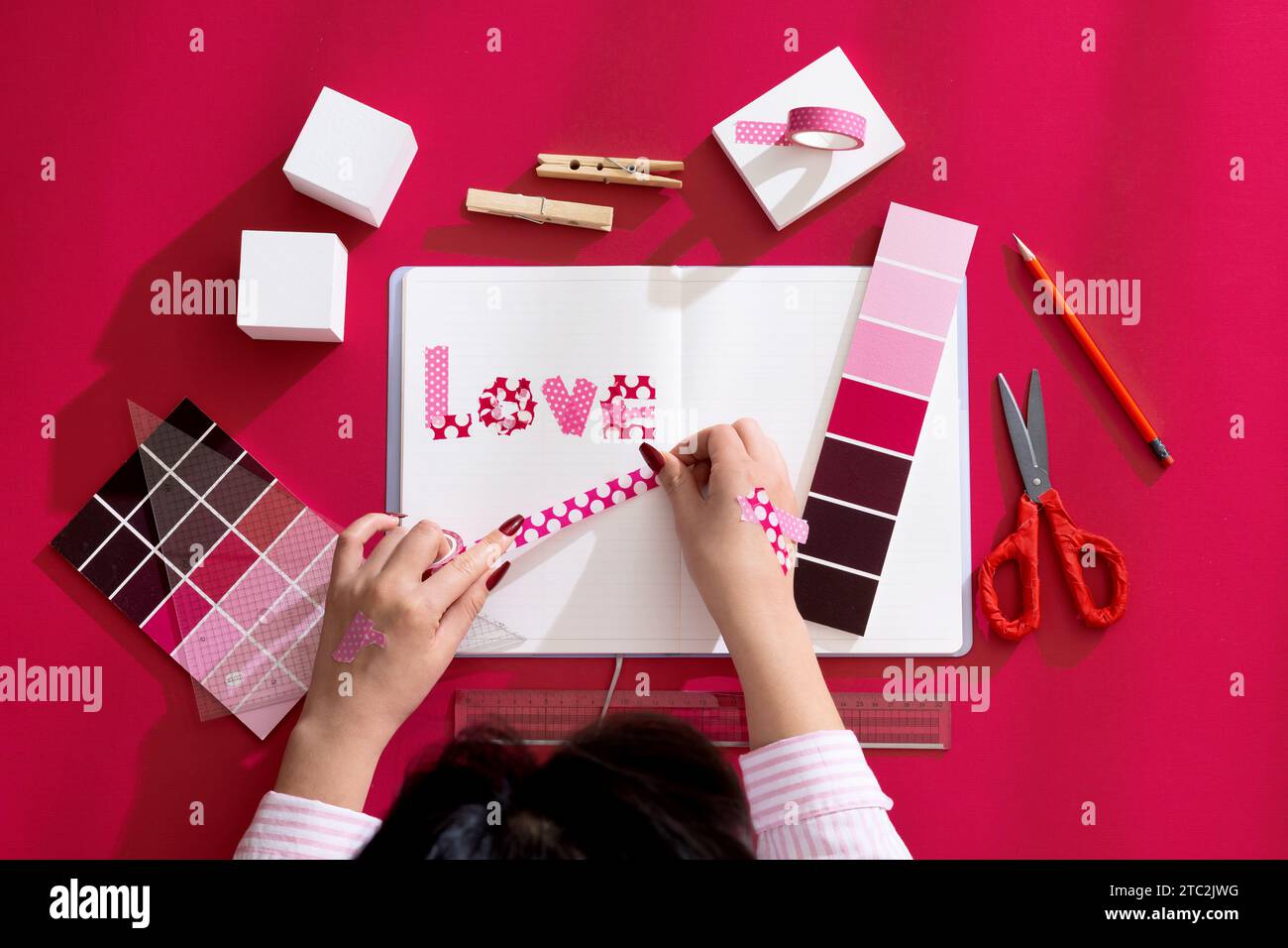 Mano di una donna che decora un diario con sfondi e oggetti di scena di colore Viva Magenta Foto Stock