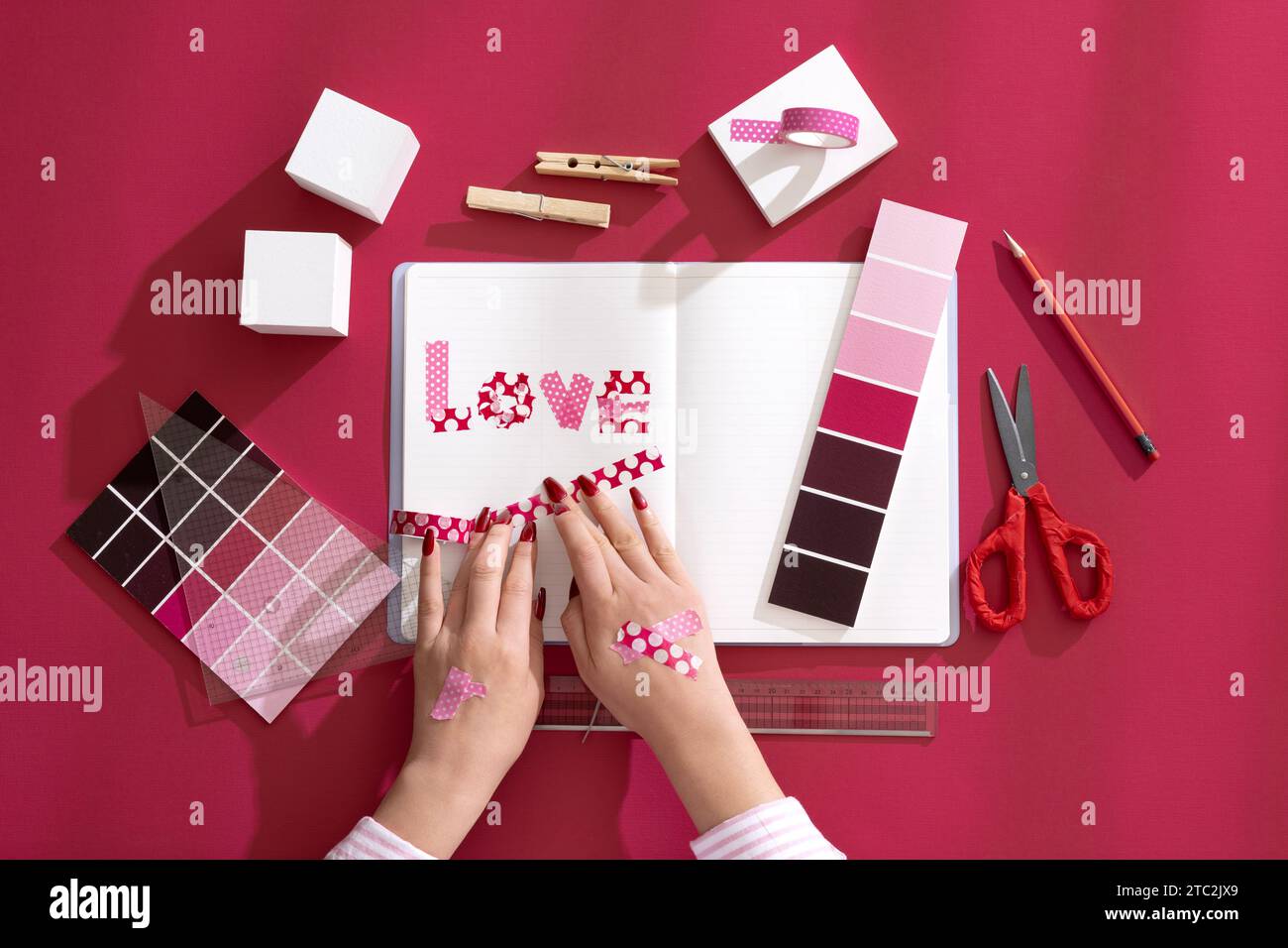 Mano di una donna che decora un diario con sfondi e oggetti di scena di colore Viva Magenta Foto Stock