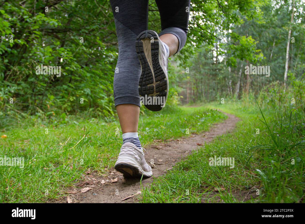 piedi di una donna che corre lungo un sentiero sterrato nel parco tra il verde Foto Stock