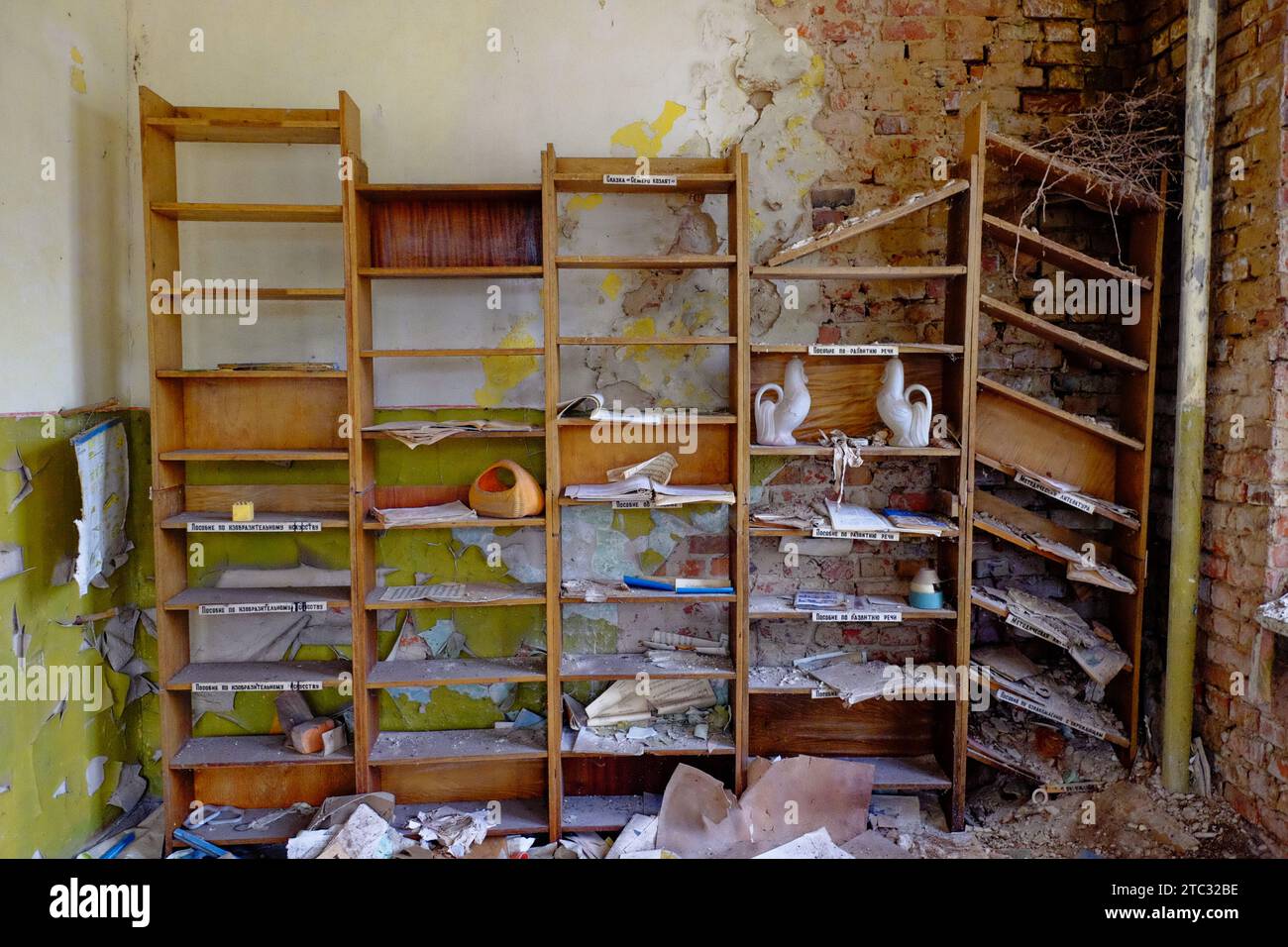 Una stanza abbandonata con una libreria di legno piena di vecchi libri e oggetti, e un muro di mattoni in rovina. Vecchi scaffali per le carte in una stanza abbandonata. Foto Stock
