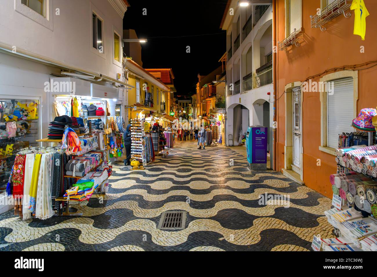 Una strada colorata di negozi e caffetterie con la pavimentazione di Calcada illuminata di notte, nella città vecchia della località balneare di Cascais in Portogallo. Foto Stock
