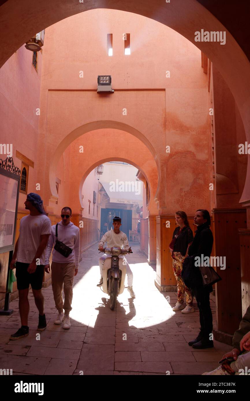 Motociclista inondato di luce sotto l'arco nella Medina di Marrakech, nota anche come Marrakech, con la Moschea in lontananza, Marocco, 10 dicembre 2023 Foto Stock