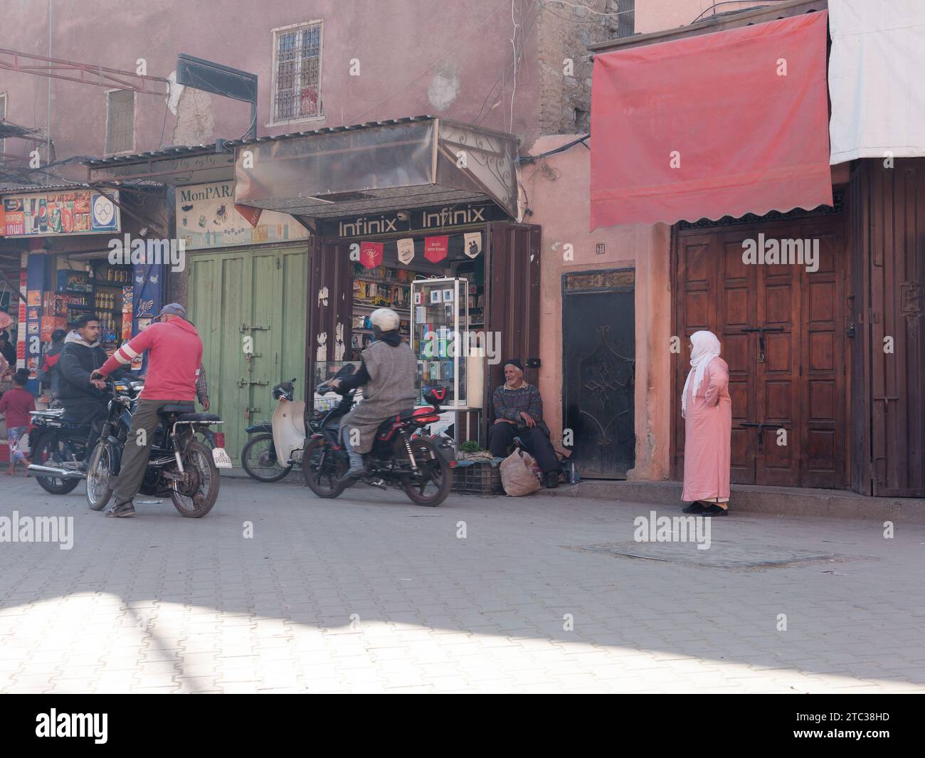 Strada con negozi e motociclette nella Medina di Marrakech, nota anche come Marrakech con la Moschea in lontananza, Marocco, 10 dicembre 2023 Foto Stock