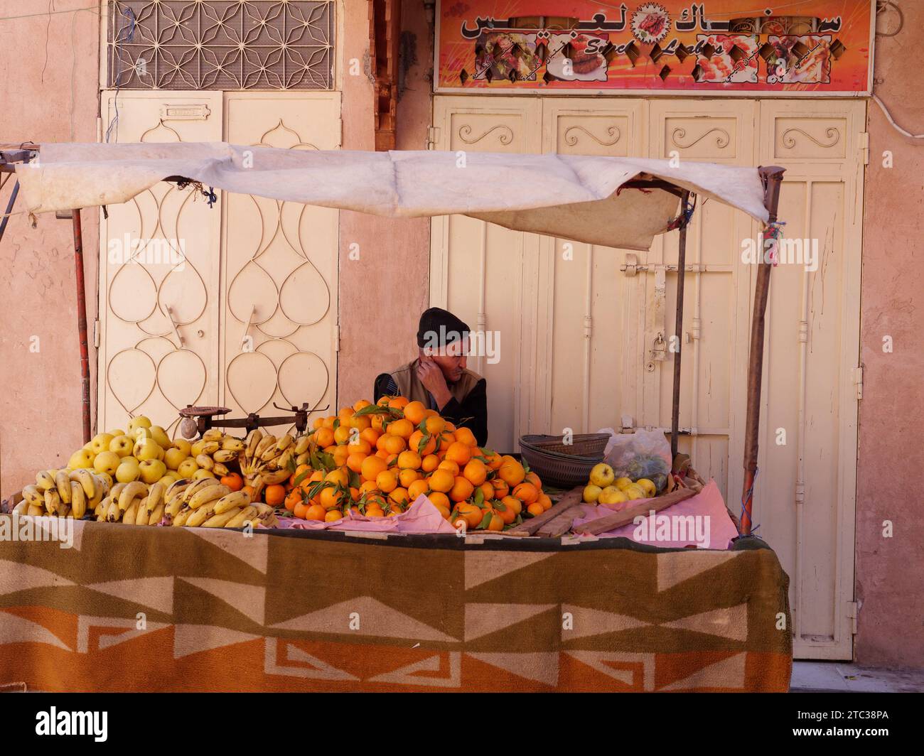 Venditore di frutta e verdura nella Medina nella città di Marrakech, alias Marrakech con la Moschea in lontananza, Marocco, 10 dicembre 2023 Foto Stock