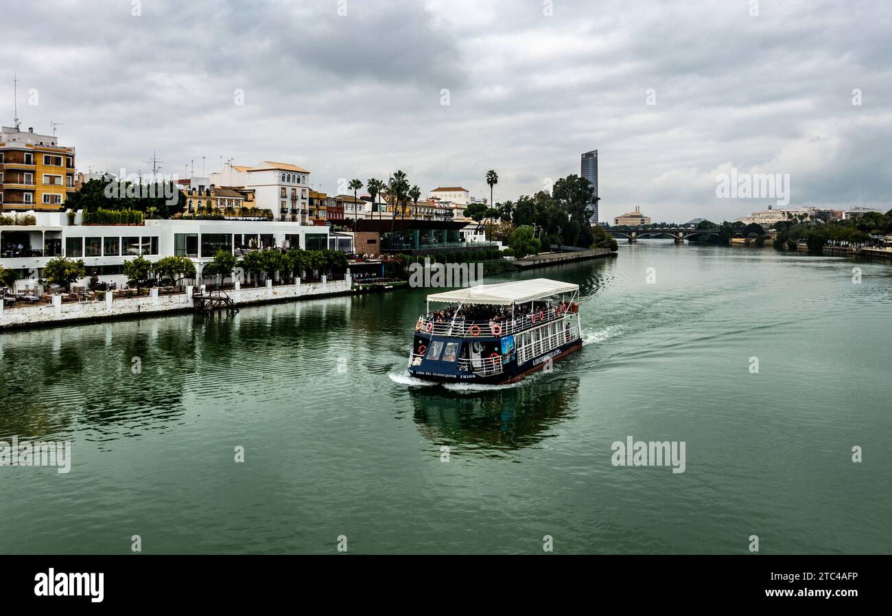 Tour in barca navigando nelle calme acque del fiume Guadalquivir, con il paesaggio urbano di Siviglia sullo sfondo. Foto Stock