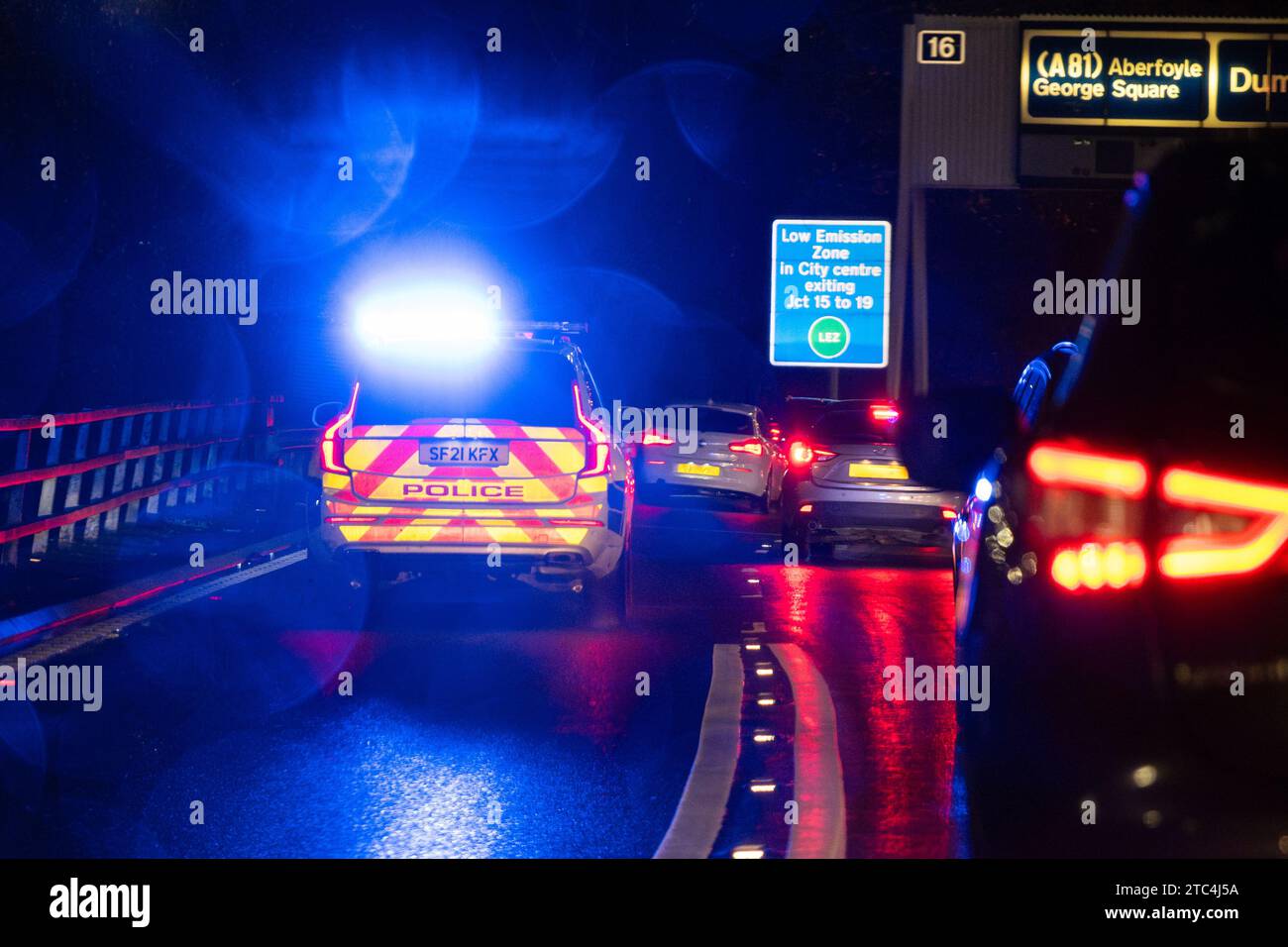 Auto della polizia con luci blu lampeggianti di notte che rispondono a un'emergenza e si uniscono al traffico pesante sull'autostrada M8 attraverso lo svincolo 15 Glasgow Scozia, Regno Unito Foto Stock