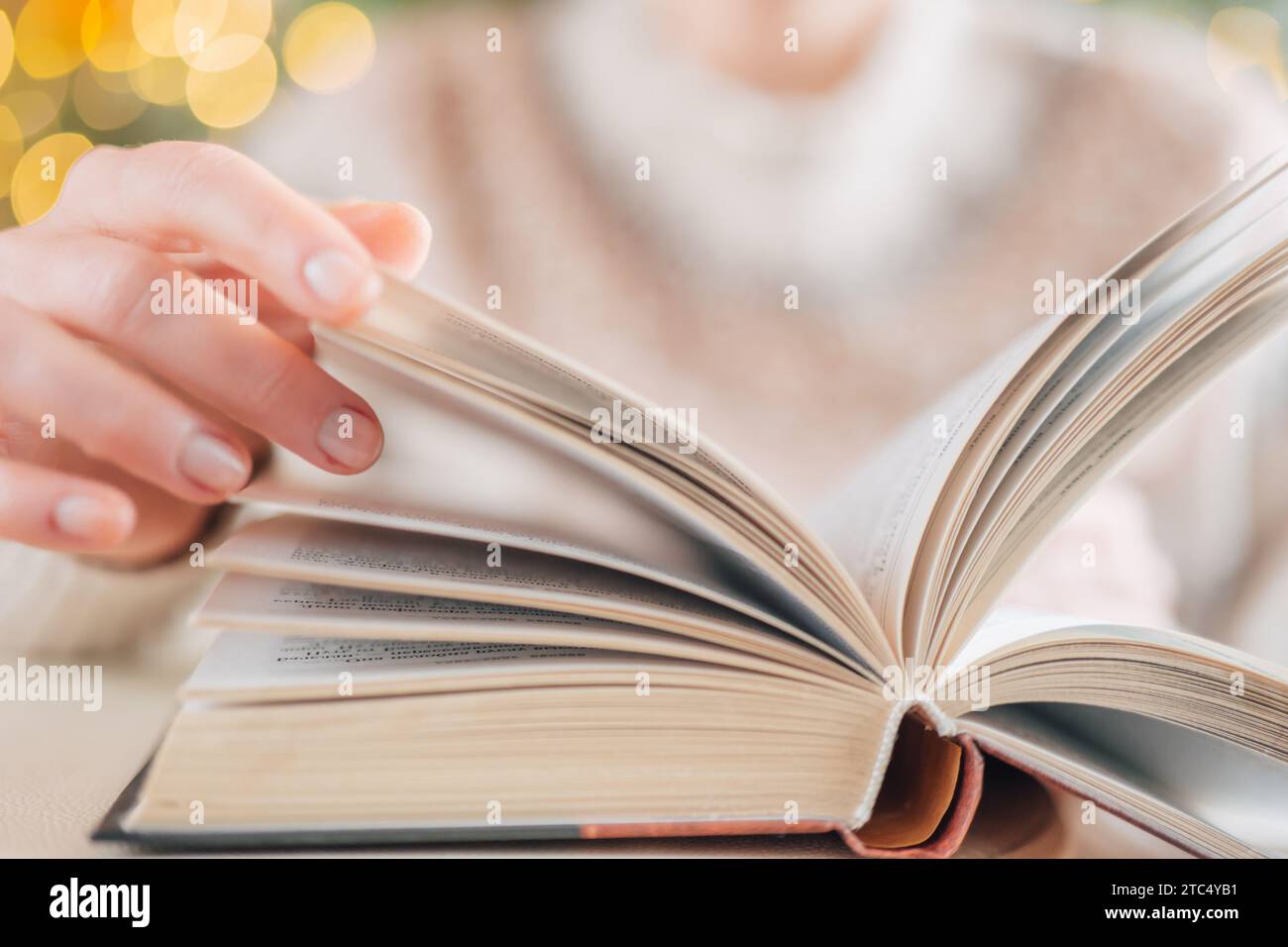 Libri di Natale.libri invernali.lettura accogliente nella stagione invernale.le mani girano le pagine di un libro sullo sfondo di ghirlande.racconti di Natale, storie, miti Foto Stock