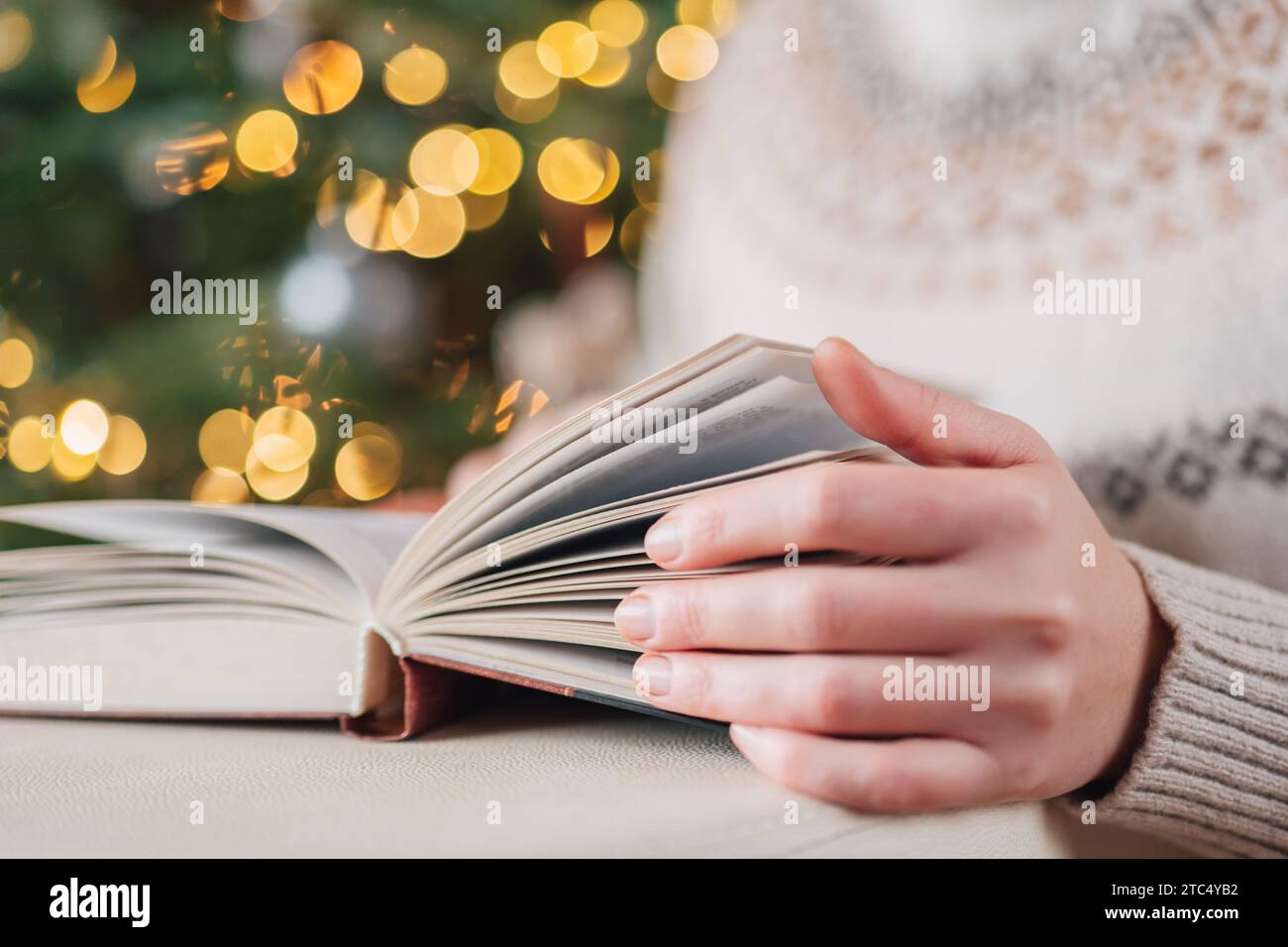 Libri di Natale.le mani girano le pagine di un libro su un albero di Natale con sfondo ghirlande.libri su temi natalizi e invernali.libri invernali.accogliente Foto Stock