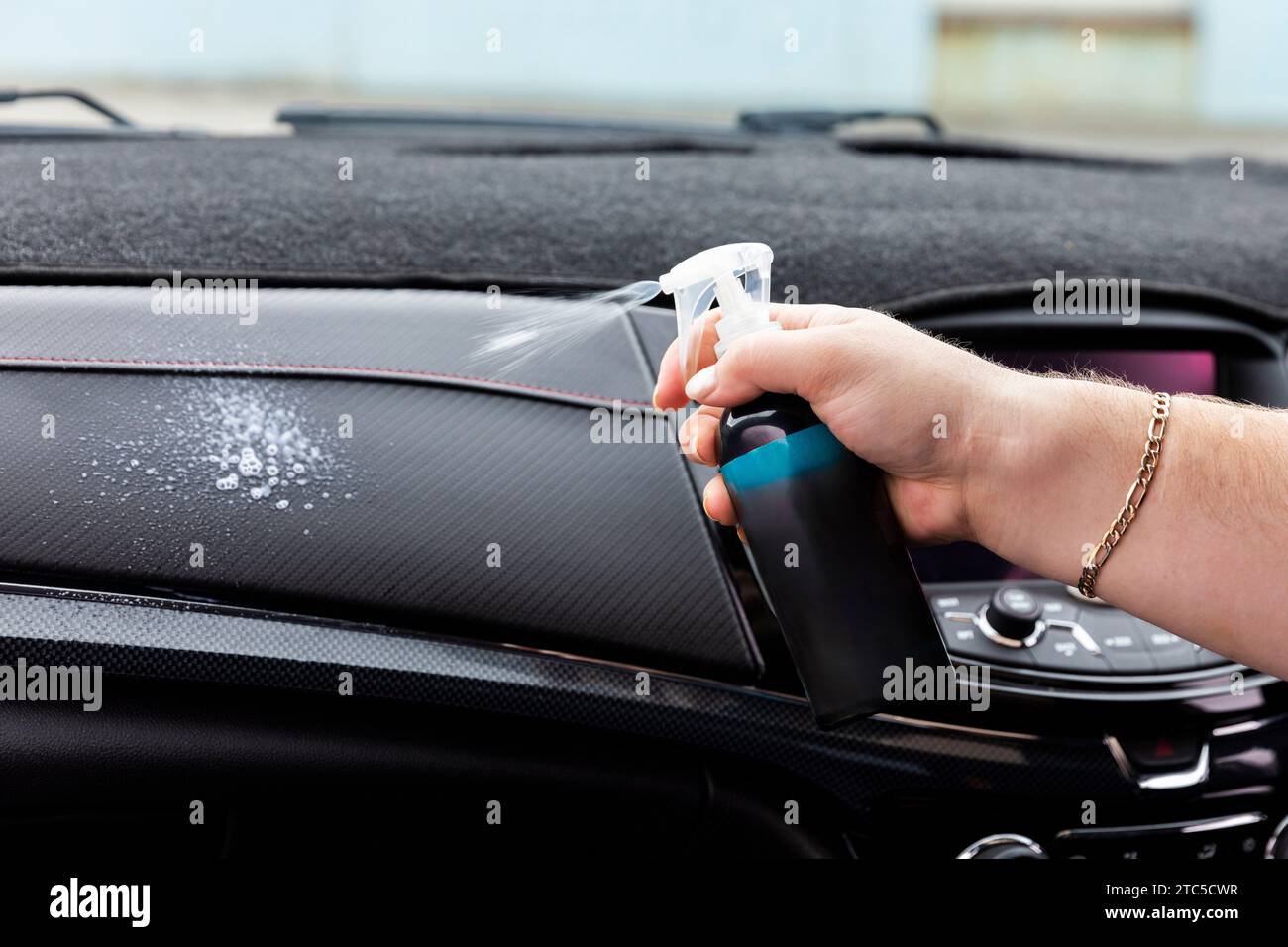 Uomo che utilizza una soluzione detergente all'interno di una vettura, rivelando la procedura di pulizia. Foto Stock