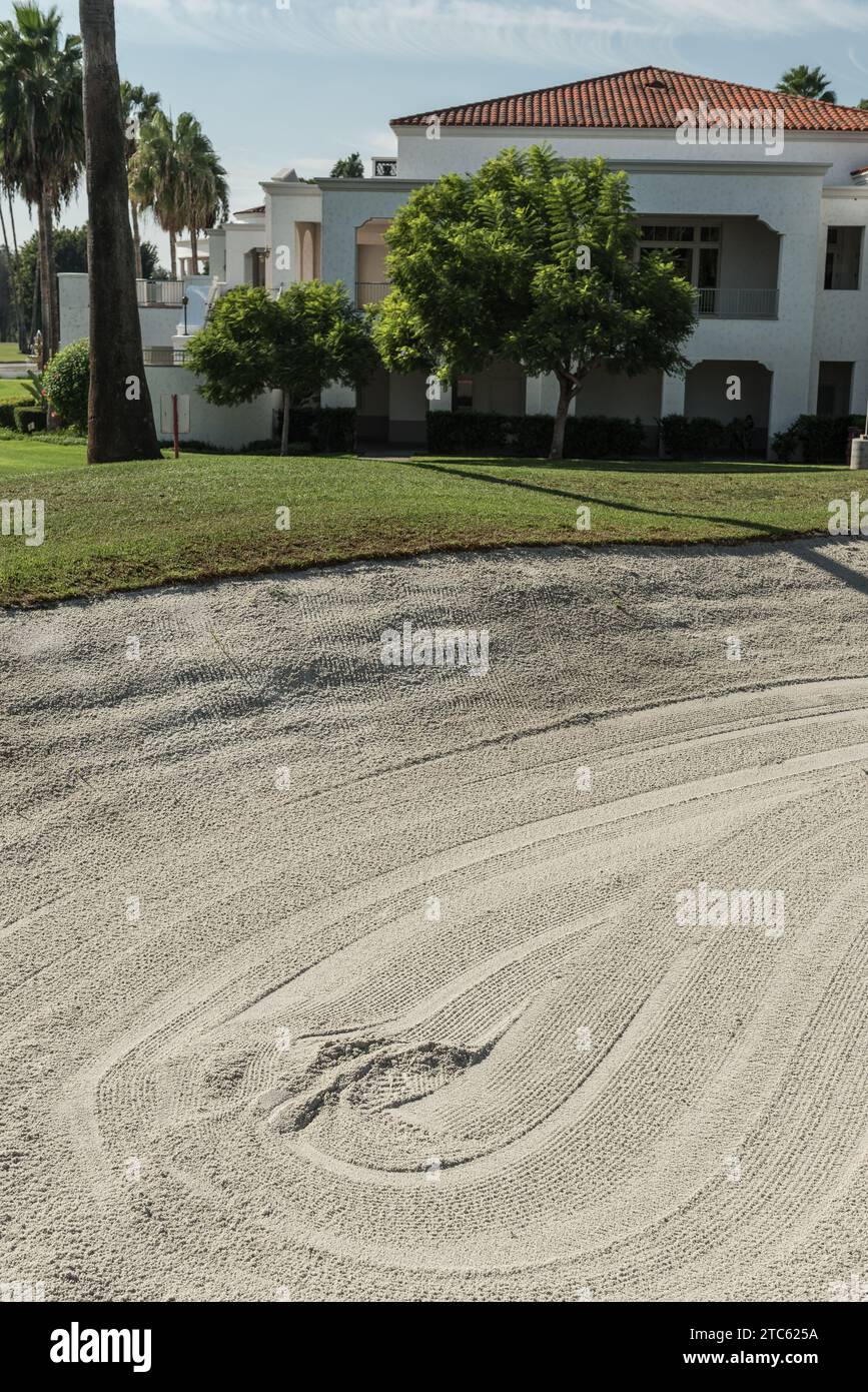Un pozzo di sabbia su un campo da golf, con una casa e un'erba verde sullo sfondo Foto Stock
