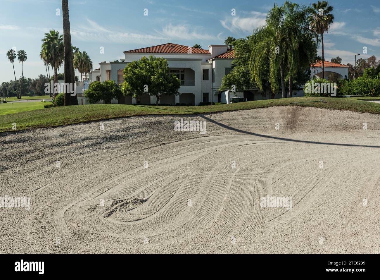 Un pozzo di sabbia su un campo da golf, con una casa e un'erba verde sullo sfondo Foto Stock