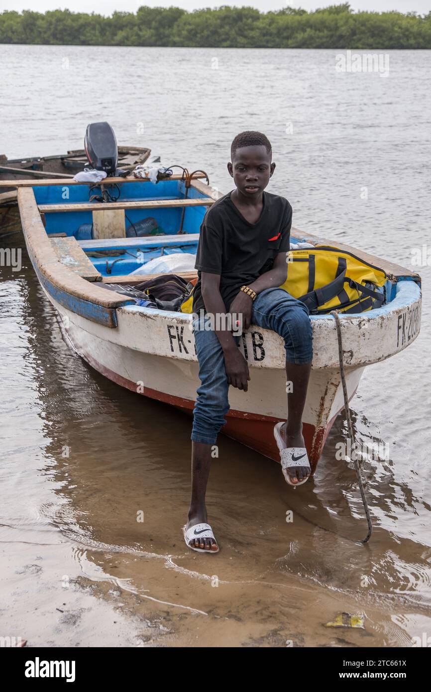 Ragazzo seduto sulla prua di una barca arenata sulla riva dei fiumi Saloum Delta, in Senegal Foto Stock