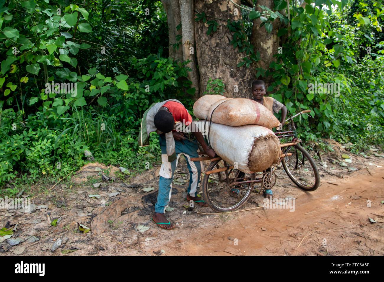 Gente dell'Africa in un posto remoto su strade sporche, prendersi cura delle merci sulle moto dopo aver attraversato il fiume, biciclette e loro teste, fotografia di strada Foto Stock