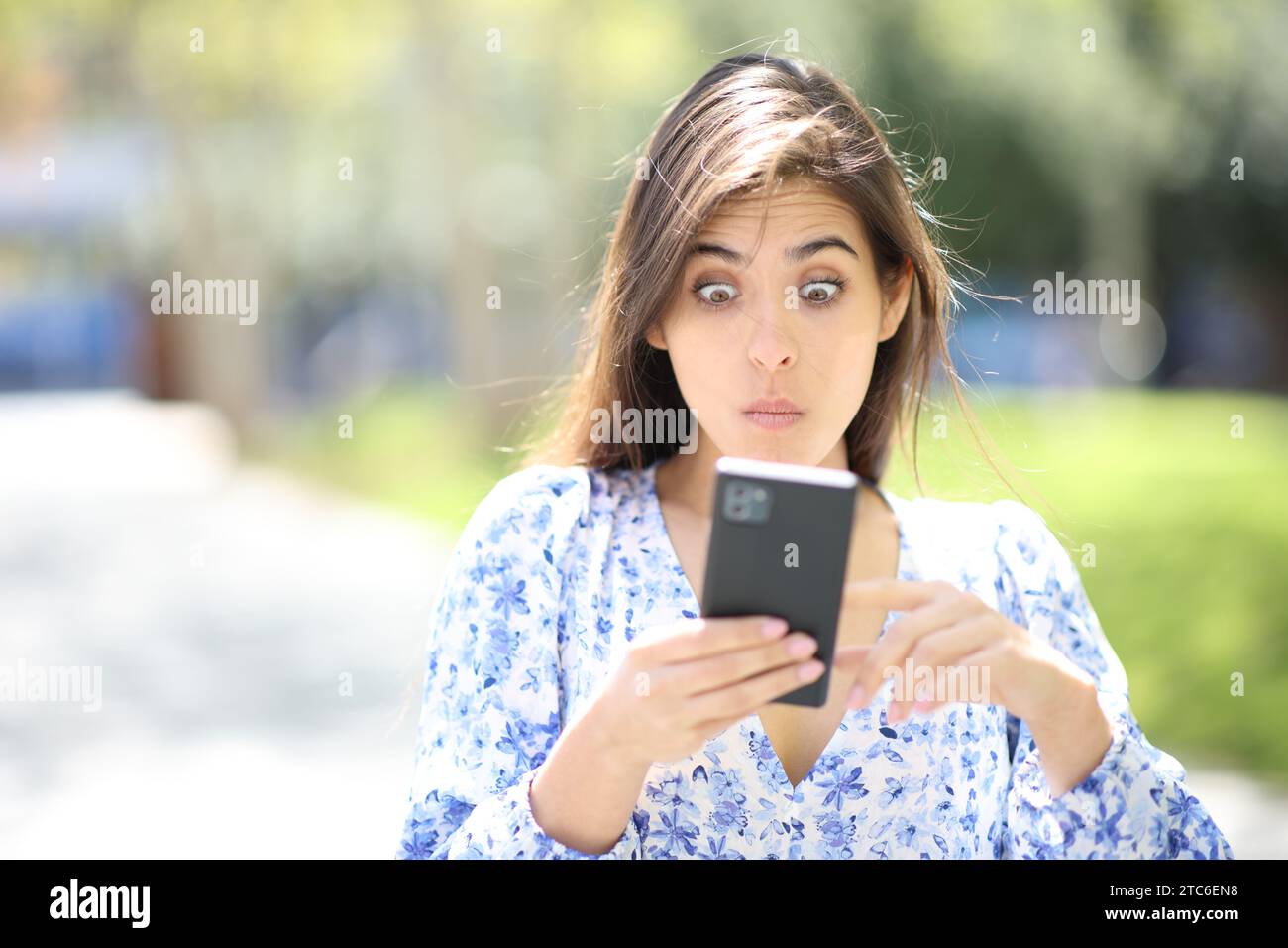 Ritratto frontale di una donna perplessa che guarda lo smartphone fuori dalla strada Foto Stock