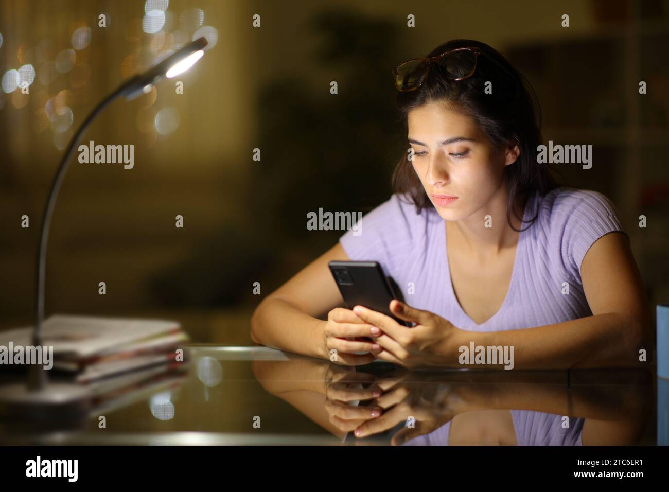 Donna seria che controlla il cellulare su una scrivania di notte a casa Foto Stock