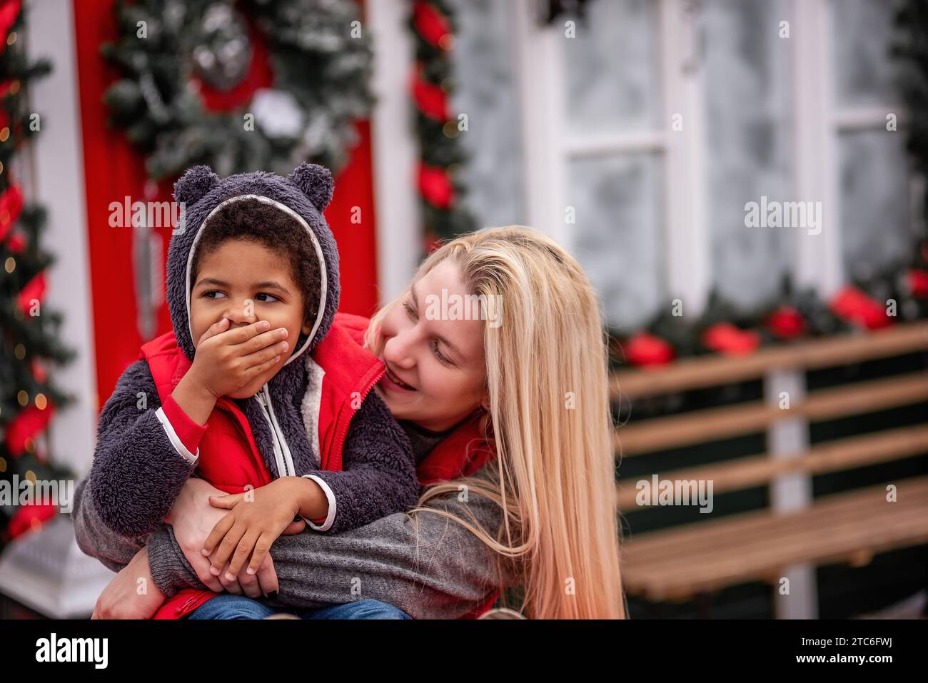 Un bambino afro-americano con madre caucasica siede sul cofano di un'auto d'epoca natalizia. Bambino con donna bionda che abbraccia, ingannando vicino al Foto Stock