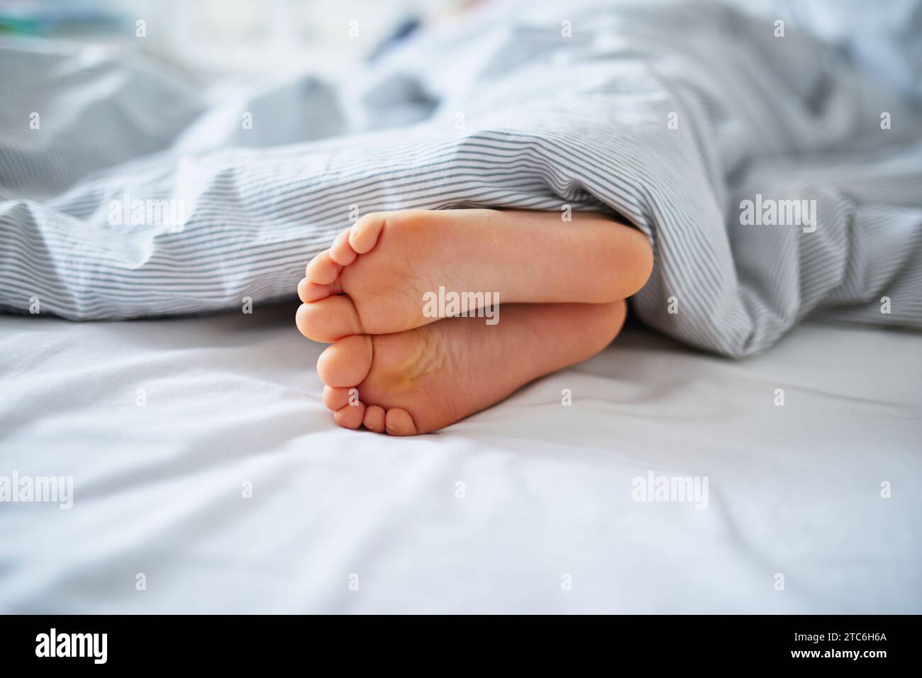 I piedi del bambino sono coperti da una coperta. Bambino che dorme in un letto comodo. La mattina presto a casa Foto Stock