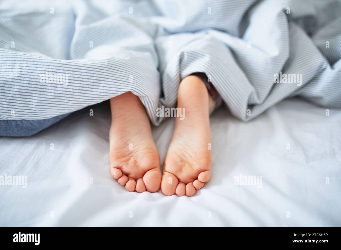 I piedi del bambino sono coperti da una coperta. Bambino che dorme in un letto comodo. La mattina presto a casa Foto Stock