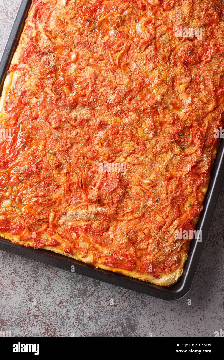 Pizza Siciliana con una morbida crosta rettangolare, una salsa di pomodoro, cipolle, acciughe e condita con pangrattato in primo piano sulla cottura Foto Stock