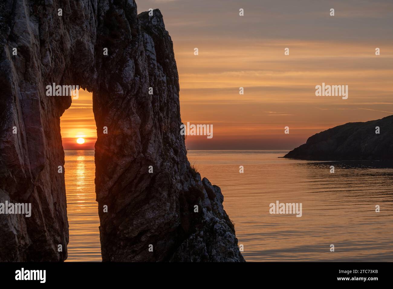 Alba attraverso un arco di roccia presso il sito vittoriano di mattoni a Porth Wen, Anglesey, Galles, Regno Unito. Primavera (maggio) 2019. Foto Stock