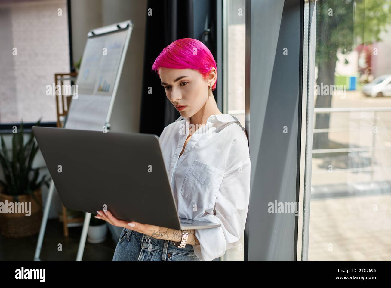 giovane donna d'affari con i capelli corti rosa che guarda il suo notebook mentre lavora in ufficio Foto Stock