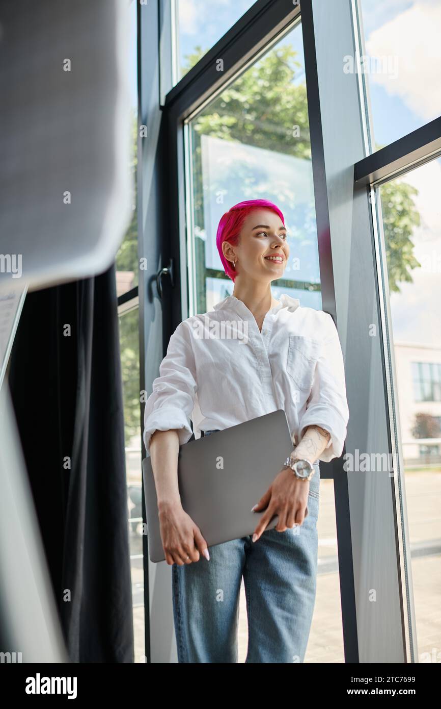 allegra giovane donna d'affari con i capelli corti rosa che tiene il portatile e guarda il suo ufficio Foto Stock