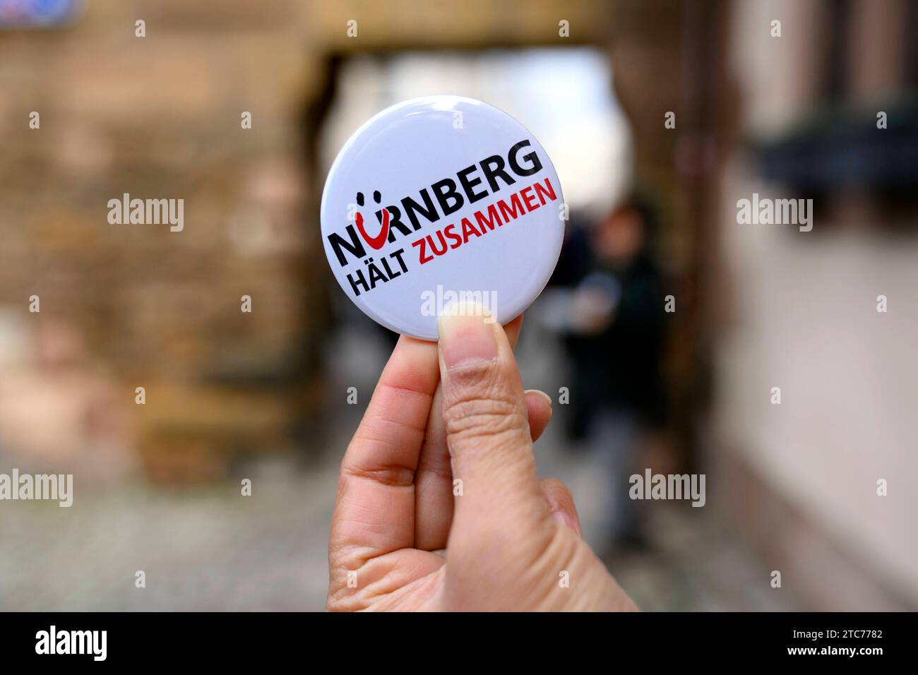 Ein button mit der Aufschrift Nürnberg hält zusammen , ein motto, unter dem ein Bündnis gesellschaftlicher Gruppen seit 2015 fr ein buntes und tolerantes Nürnberg wirbt. ALS Aktion zum 75. Jahrestag der Verkündung der Allgemeinen Erklärung der Menschenrechte bilden Teilnehmer eine Menschenkette in der Straße der Menschenrechte. Auf den Säulen in der Straße sind die 30 Artikel der un-Menschenrechtscharta in verschiedenen Sprachen zu lesen. Nürnberg, 10.12.2023 Bayern Deutschland *** Un bottone con l'iscrizione Norimberga si attacca insieme, un motto sotto il quale un'alleanza di gruppi sociali ha ape Foto Stock