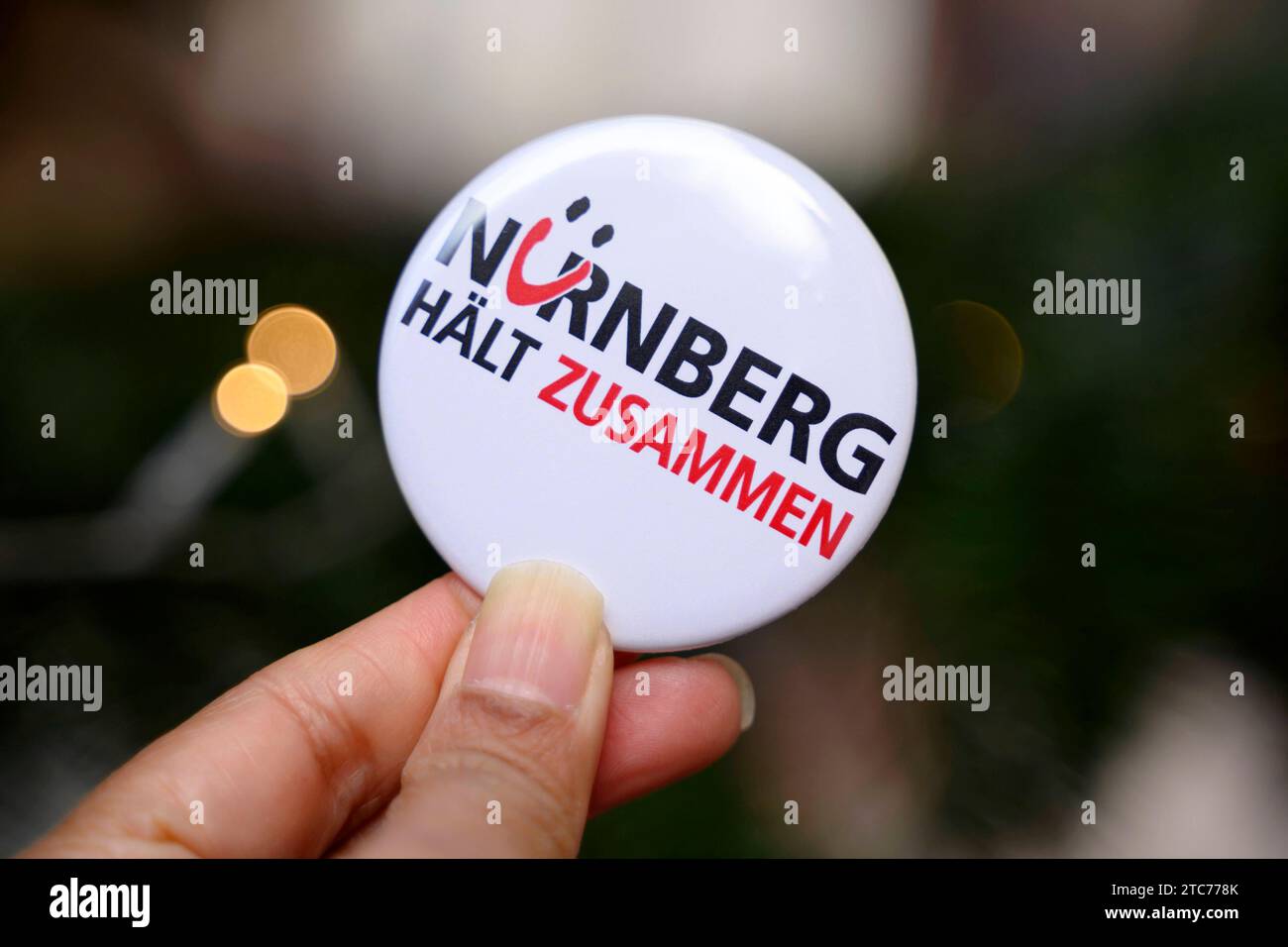 Ein button mit der Aufschrift Nürnberg hält zusammen , ein motto, unter dem ein Bündnis gesellschaftlicher Gruppen seit 2015 fr ein buntes und tolerantes Nürnberg wirbt. ALS Aktion zum 75. Jahrestag der Verkündung der Allgemeinen Erklärung der Menschenrechte bilden Teilnehmer eine Menschenkette in der Straße der Menschenrechte. Auf den Säulen in der Straße sind die 30 Artikel der un-Menschenrechtscharta in verschiedenen Sprachen zu lesen. Nürnberg, 10.12.2023 Bayern Deutschland *** Un bottone con l'iscrizione Norimberga si attacca insieme, un motto sotto il quale un'alleanza di gruppi sociali ha ape Foto Stock