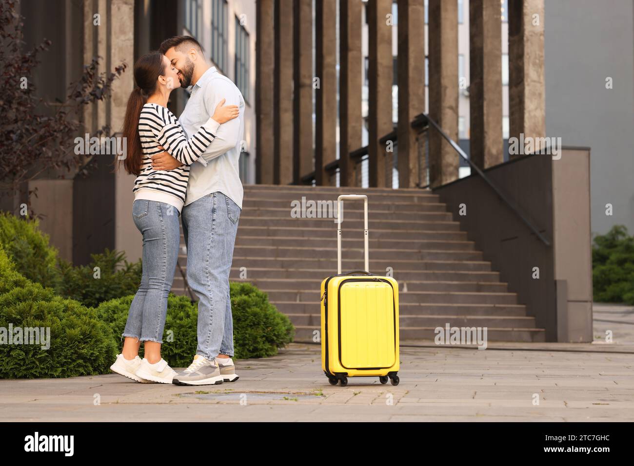 Relazione a distanza. Bellissime coppie giovani che si baciano e le valigie vicino a un edificio all'aperto Foto Stock