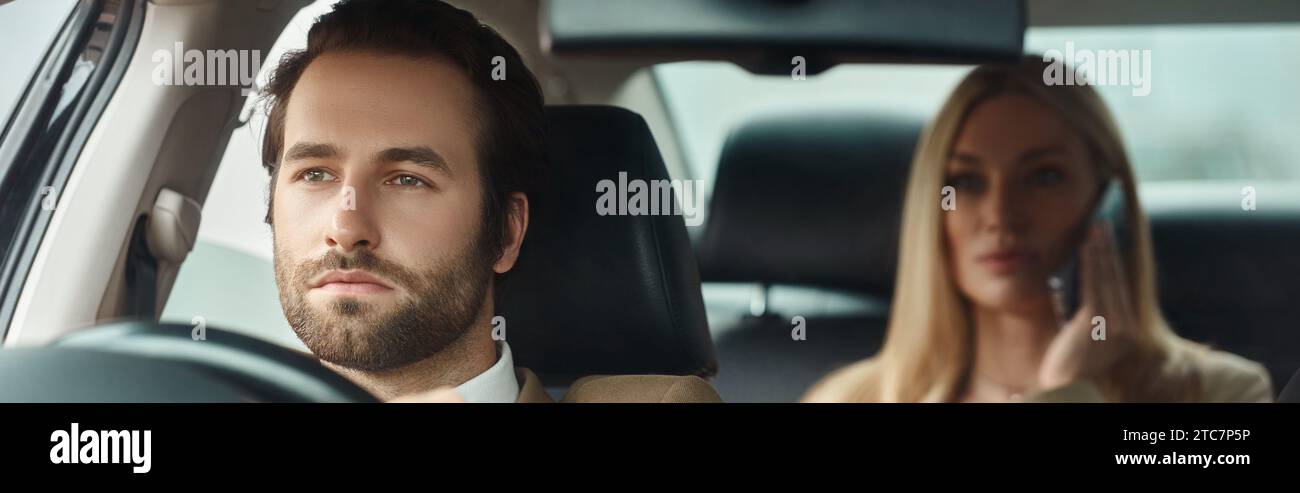 bell'uomo barbuto che guida un'auto con una donna d'affari bionda che parla al telefono cellulare, striscione Foto Stock