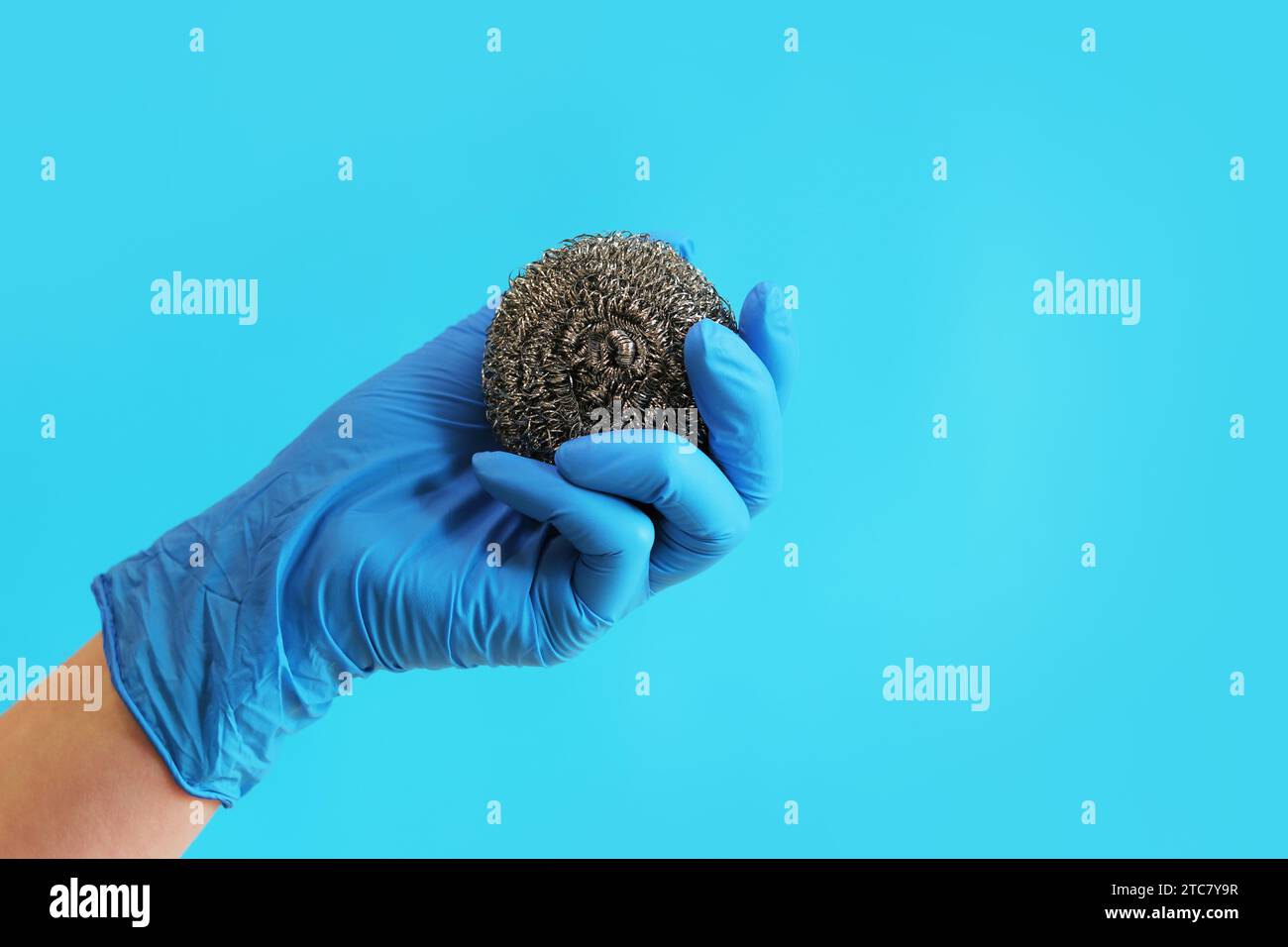 Spazzola da cucina in acciaio inox. Attrezzi per la pulizia del barbecue. Una mano in un guanto blu lattice contiene una spazzola a sfera in acciaio inox. Spazzola lavastoviglie, cucina a. Foto Stock