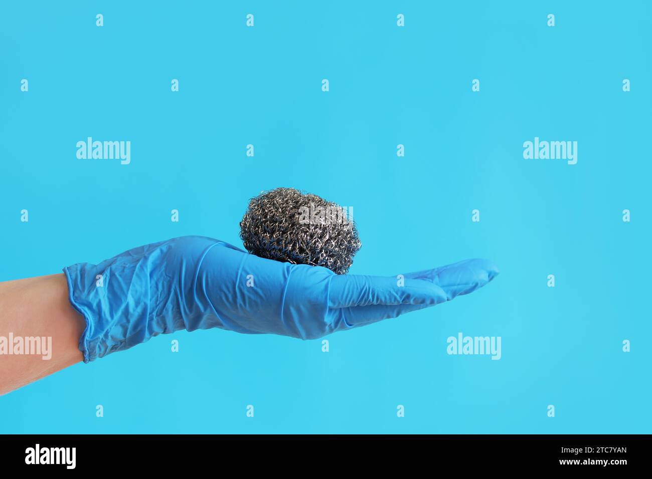 Spazzola da cucina in acciaio inox. Attrezzi per la pulizia del barbecue. Una mano in un guanto blu lattice contiene una spazzola a sfera in acciaio inox. Spazzola lavastoviglie, cucina a. Foto Stock