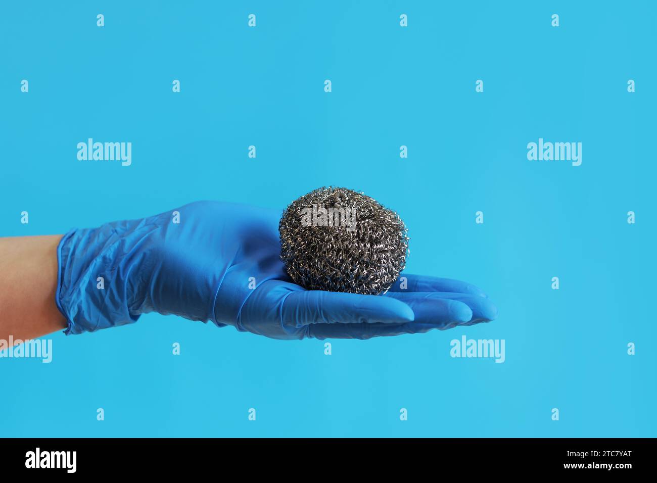 Spazzola da cucina in acciaio inox. Attrezzi per la pulizia del barbecue. Una mano in un guanto blu lattice contiene una spazzola a sfera in acciaio inox. Spazzola lavastoviglie, cucina a. Foto Stock