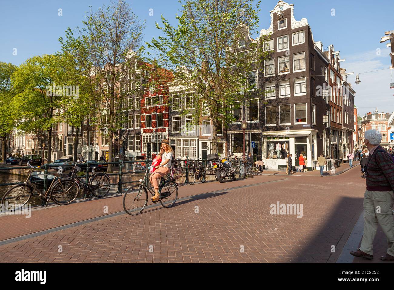 Giovane donna che va in bicicletta e parla al telefono su un ponte ad Amsterdam. Foto Stock