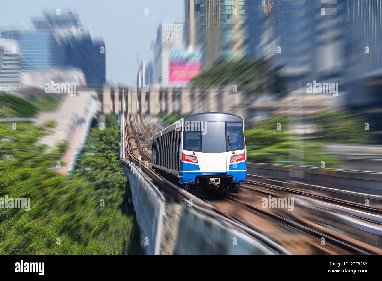 Il treno elettrico sfoca la velocità di movimento tra gli alberi e un parco in una metropoli. Foto Stock