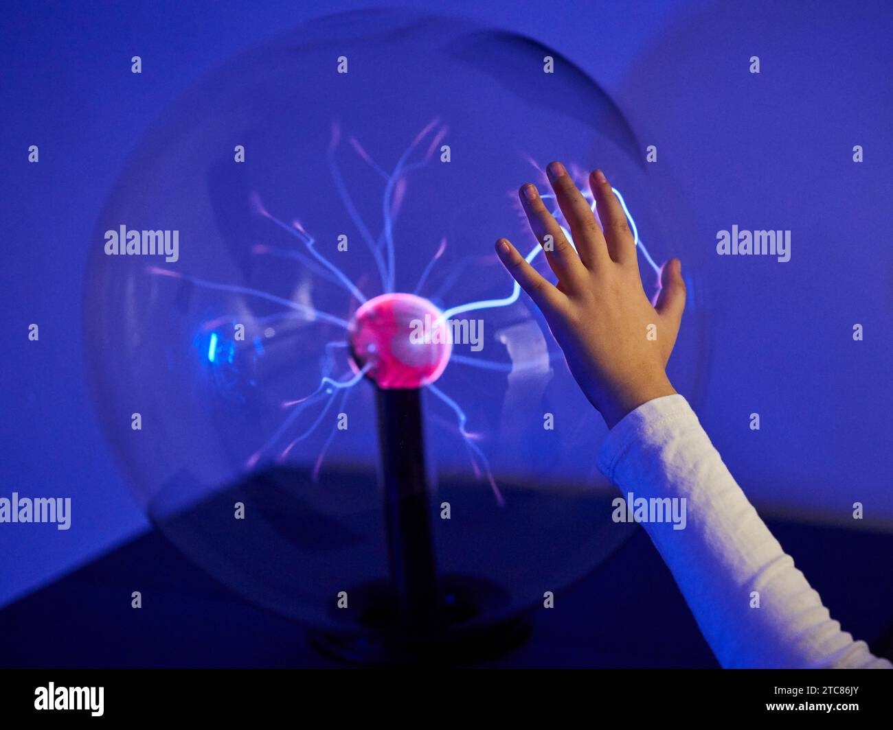 Una persona che interagisce con una palla di elettricità blu in un ambiente buio. Foto Stock