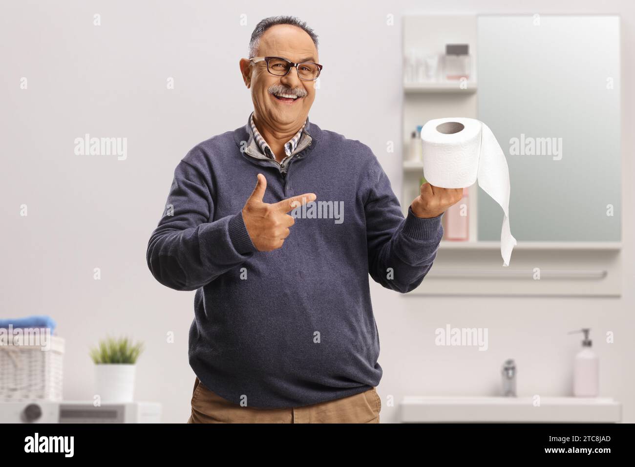 Uomo maturo sorridente che punta un rotolo di carta igienica all'interno di un bagno Foto Stock