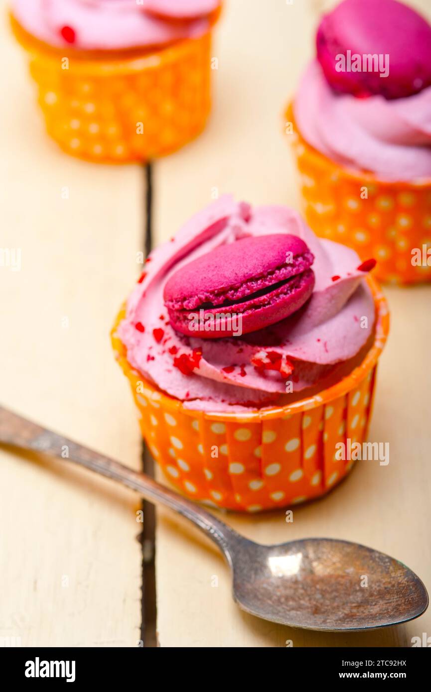 Fresco cupcake rosa alla crema di bacca con macaroon sopra tavola rustica di legno Foto Stock