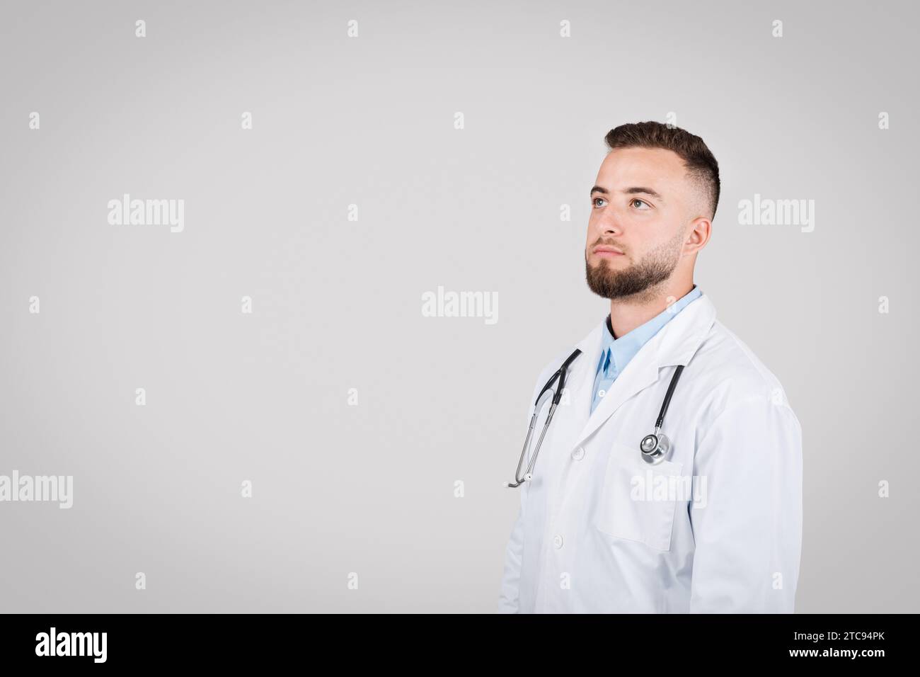 Medico maschio sicuro di sé in camice bianco che guarda verso l'alto lo spazio libero Foto Stock