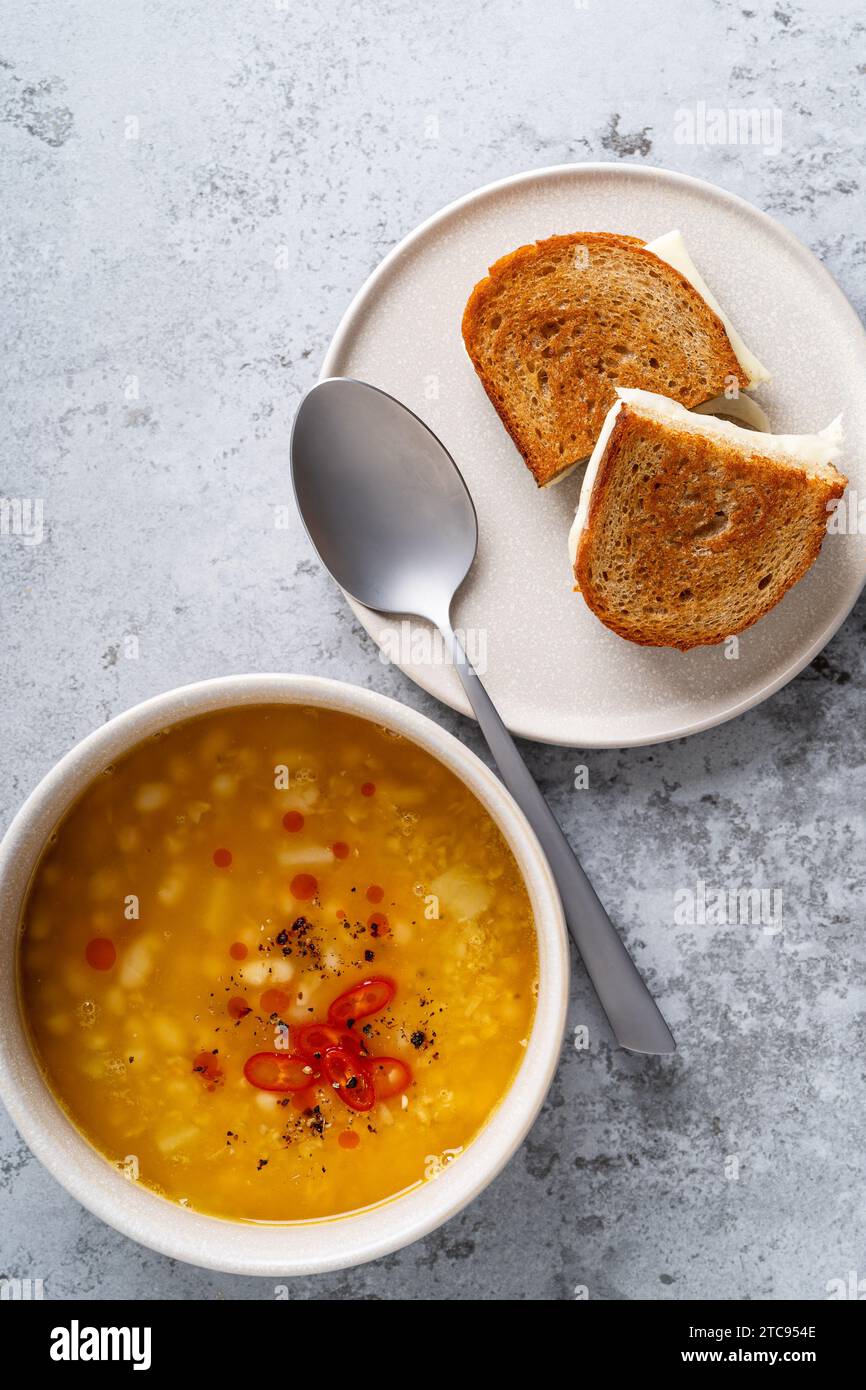 Ciotola di zuppa di fagioli bianchi con sandwich di formaggio di pane di segale su sfondo grigio, cibo salutare e confortevole, vista dall'alto Foto Stock