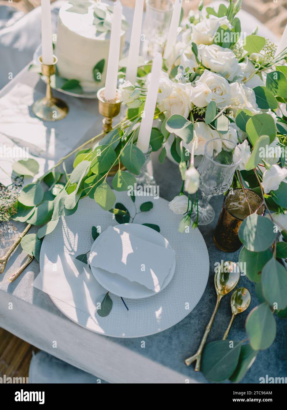 Elegante tavolo con una carta bianca decorata con rami di eucalipto. Matrimonio Mockup. Tavolo romantico con biglietto d'invito di carta. Foto Stock