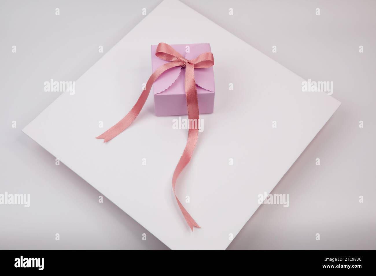 Un'immagine di un regalo rosa, avvolto da un fiocco di nastro bianco, su uno sfondo bianco nitido Foto Stock
