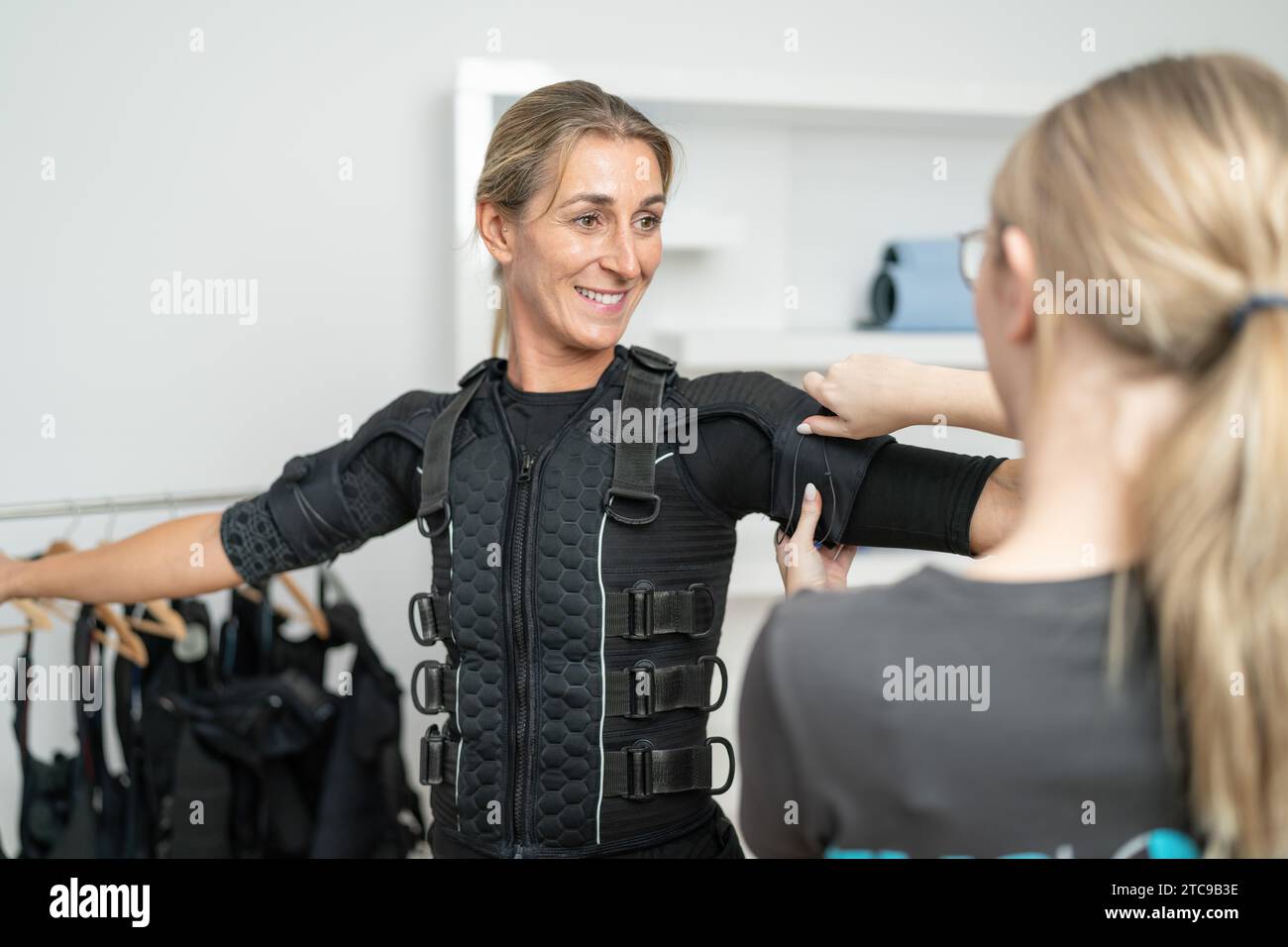 Il formatore assiste una cliente femminile indossando un tuta da addestramento EMS o un esercizio di addestramento in uno studio EMS Foto Stock