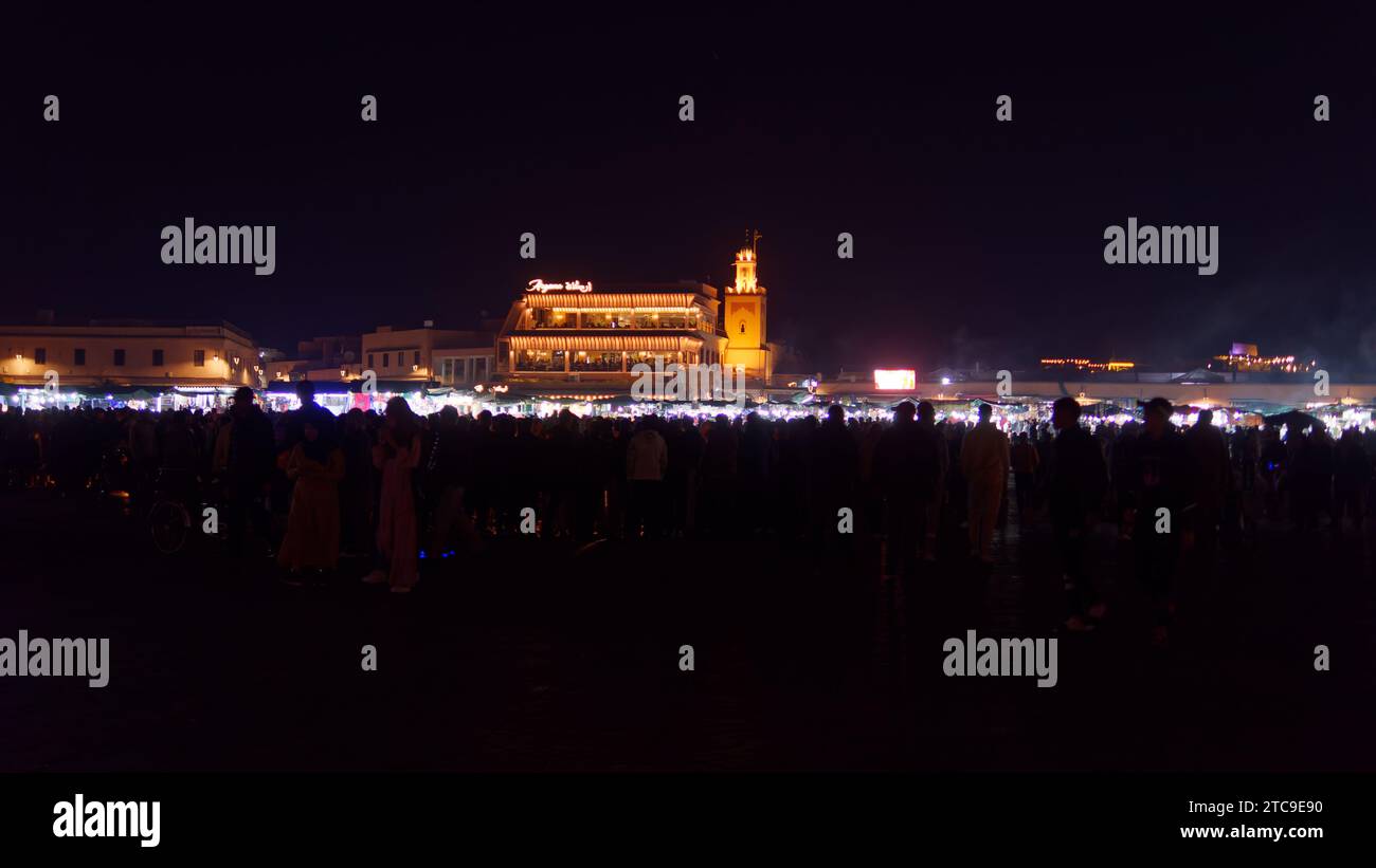 Folle in Piazza Jemaa el-Fna di notte con un ristorante illuminato da inondazioni dorate nella città di Marrakech, alias Marrakech, Marocco, 11 dicembre 2023 Foto Stock