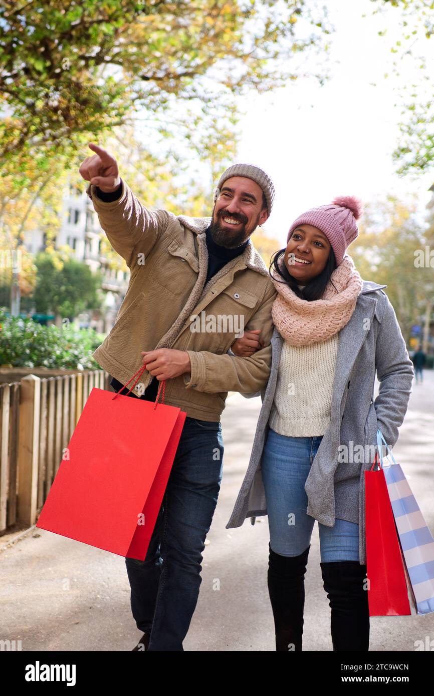 Coppia multirazziale che cammina in città facendo shopping di natale insieme, indicando le cose. Foto Stock