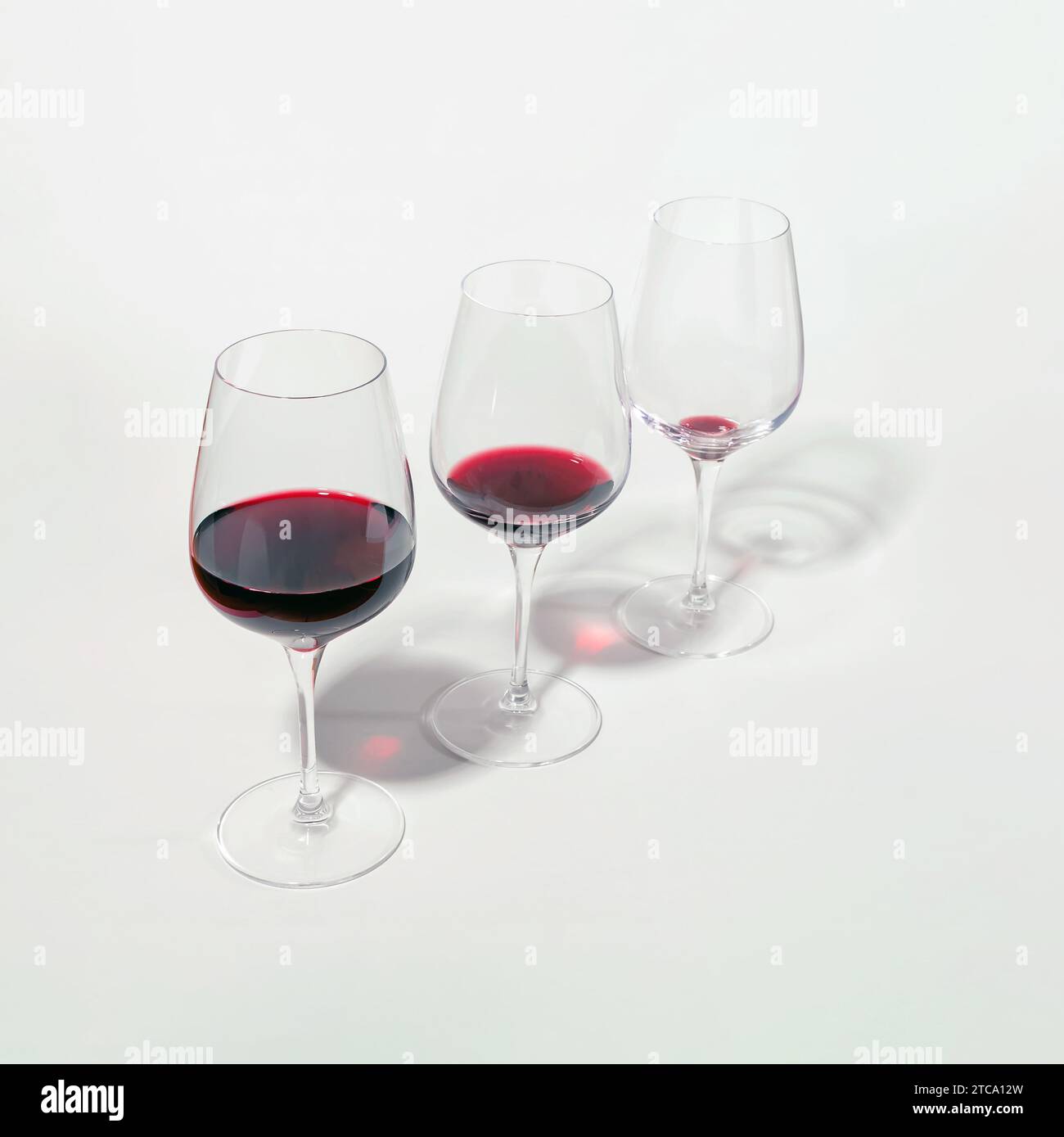 Tre bicchieri con livelli di vino rosso abbassati, isolati su bianco. Concetto di consumo consapevole e riduzione dell'alcol. Foto Stock