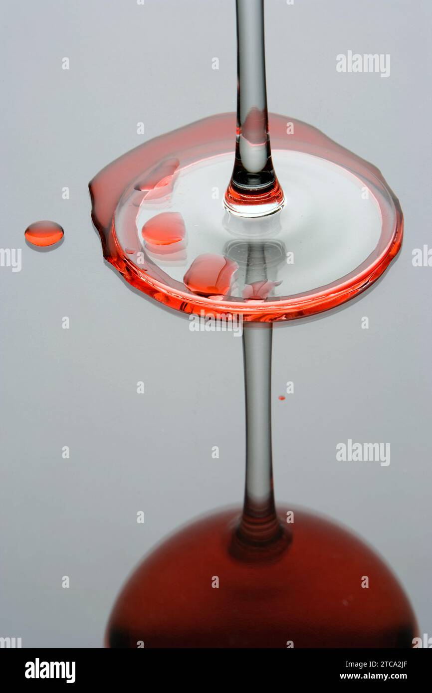 La riflessione di un bicchiere di vino rosso con vino versato su sfondo grigio Foto Stock