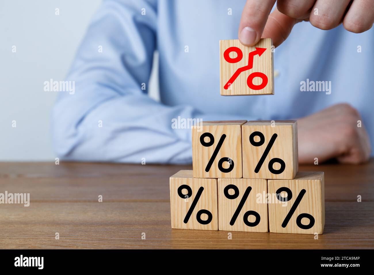 Aumento del tasso ipotecario illustrato da segni di percentuale con freccia verso l'alto. Uomo che costruisce una piramide di cubi su un tavolo di legno, primo piano Foto Stock